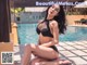 A woman in a black bikini sitting by a pool.