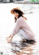 A woman in a pink sweater and hat crouching in the water.