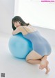 A woman in a blue bodysuit sitting on a blue ball.