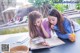 Two young women sitting at a table reading a book.