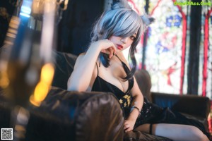 A woman in a black dress sitting on a couch.